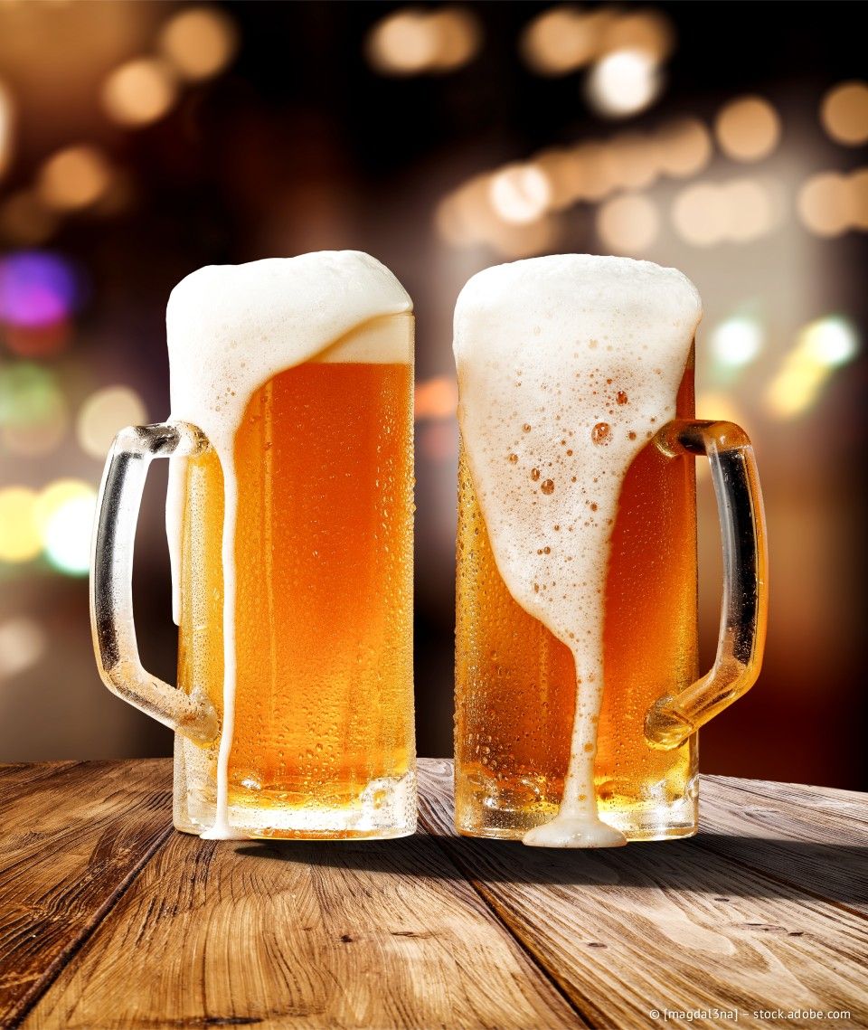 Zwei überquellende Bierkrüge auf einem Holztisch, im Hintergrund ein verschwommener Lichteffekt.