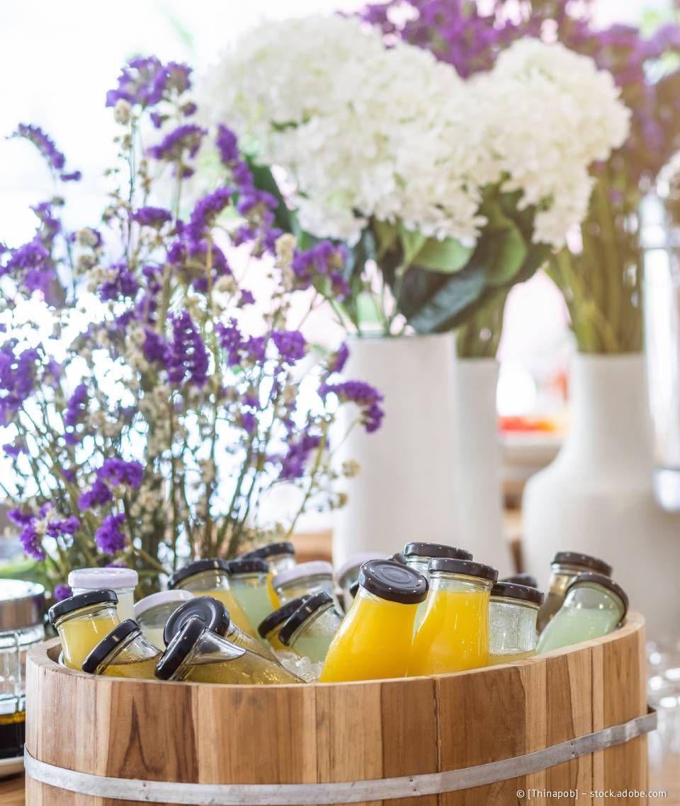 Eisbehälter aus Holz mit abgefüllten Getränken, lila und weiße Blumen in Vasen.
