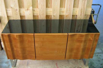 Vor einem Holzzaun steht ein Holzschrank mit schwarzer Oberseite.