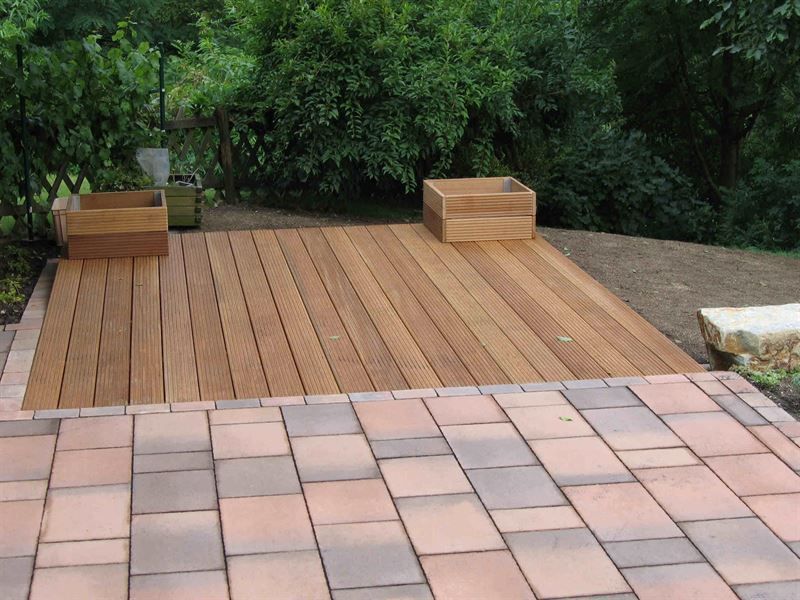 Ein Holzdeck ist von Ziegeln und Bäumen umgeben