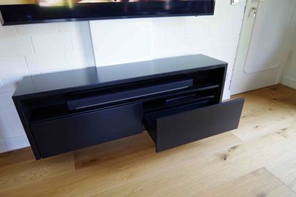 Ein schwarzes Entertainment-Center mit einer geöffneten Schublade in einem Wohnzimmer.