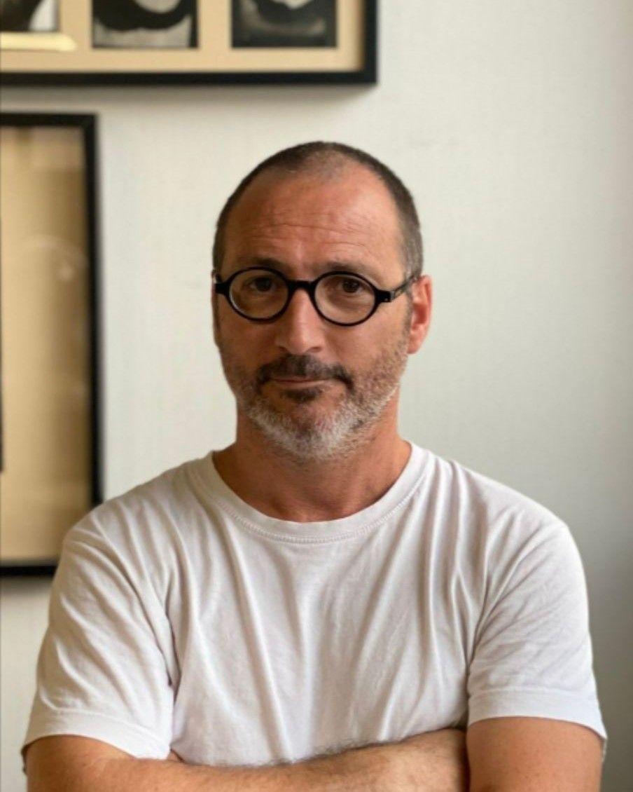 Un hombre con gafas y camisa blanca está de pie con los brazos cruzados.