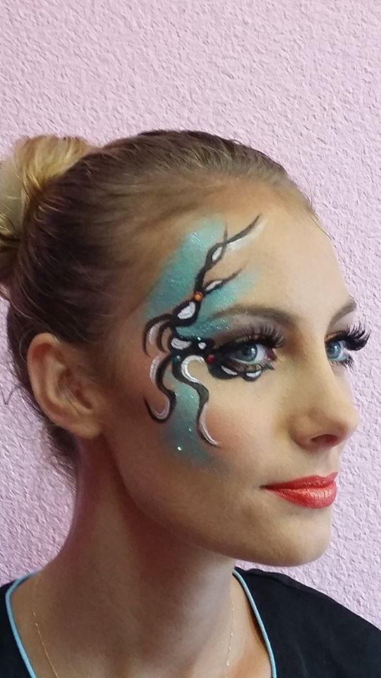 Femme au maquillage facial élaboré, comprenant des éléments turquoise, noirs et argentés. Rouge à lèvres rouge.