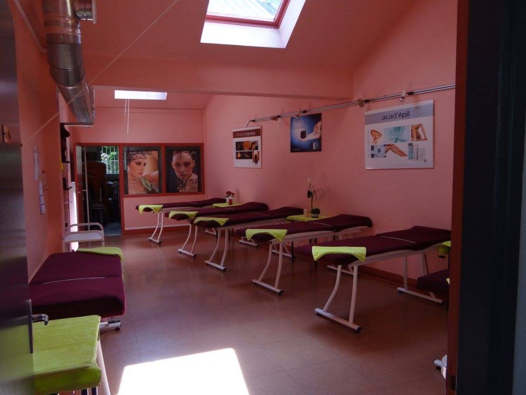 Une salle de soins avec des tables de massage, des affiches sur les murs roses et une verrière.