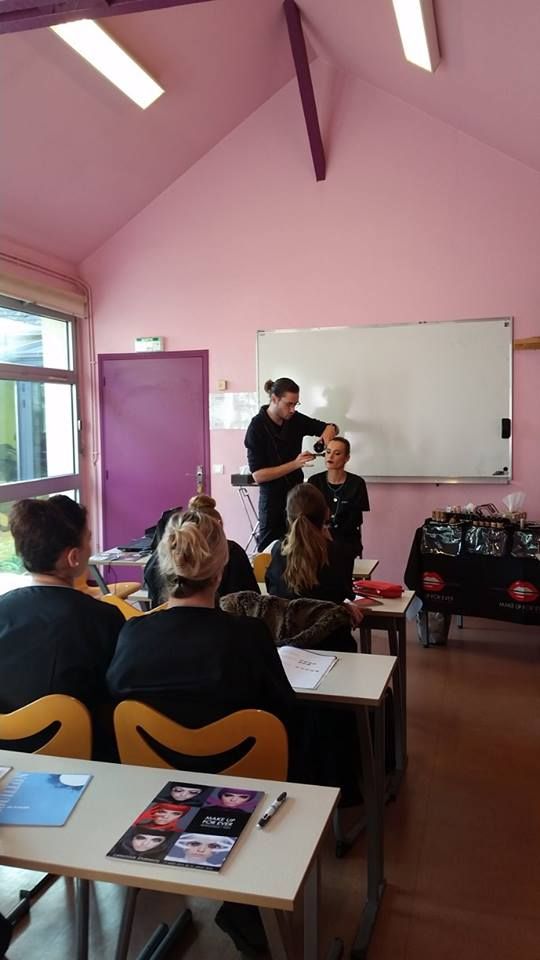 Cours de coiffure : le professeur fait une démonstration sur un mannequin dans une salle de classe rose, les élèves regardent.