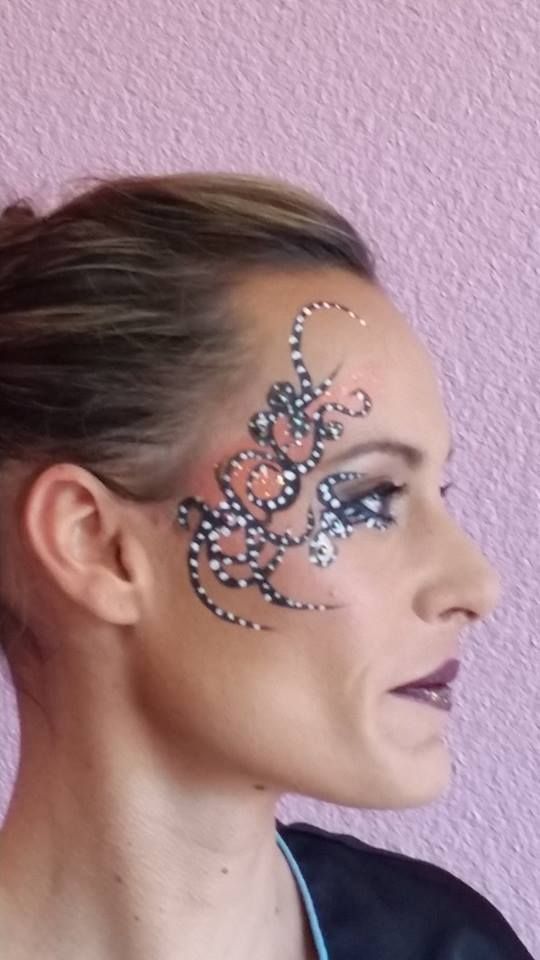 Femme au visage maquillé de spirales et de points, près des yeux et sur le front. Rouge à lèvres foncé, fond rose.