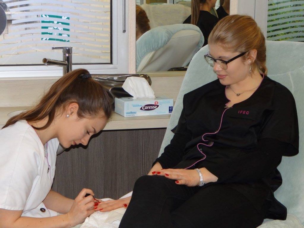 Une personne se fait vernir les ongles dans un salon. Une autre personne applique du vernis à ongles.