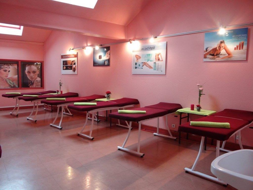 Salle de spa rose avec tables de massage, posters et lavabo.