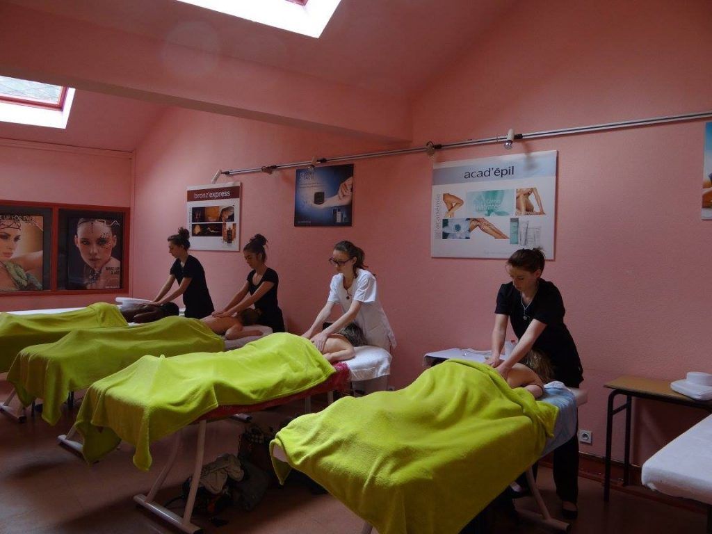 Des personnes se font masser le dos par des masseuses dans une pièce rose.