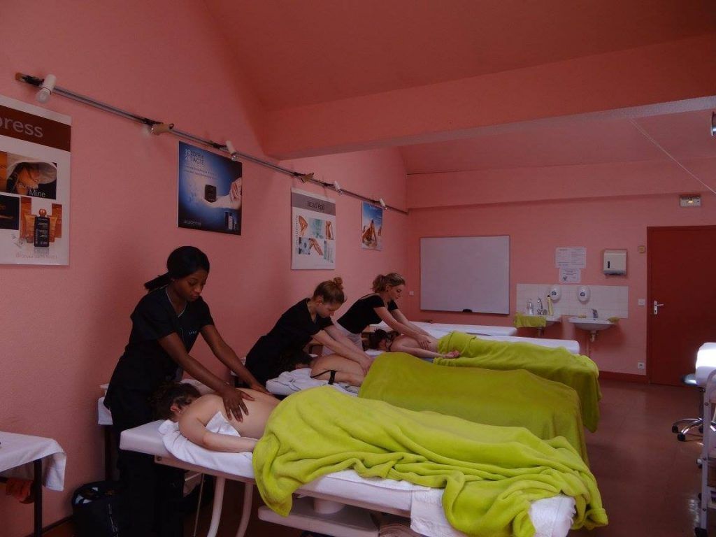 Des étudiants en massothérapie s'exercent sur des clients dans une salle de classe aux murs roses.