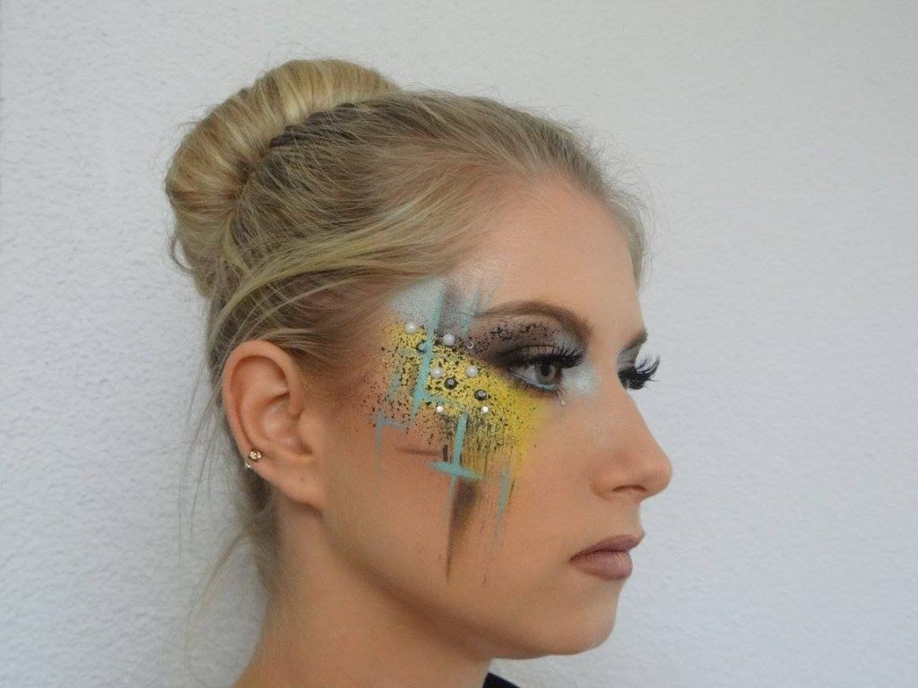 Femme au maquillage des yeux créatif, avec des touches de jaune, de bleu et de noir, les cheveux en chignon.