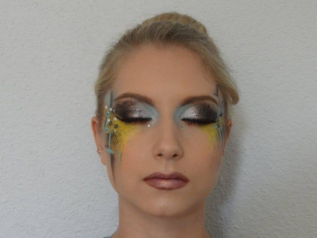 Femme au maquillage des yeux élaboré ; détails bleus, jaunes et noirs sur son visage.