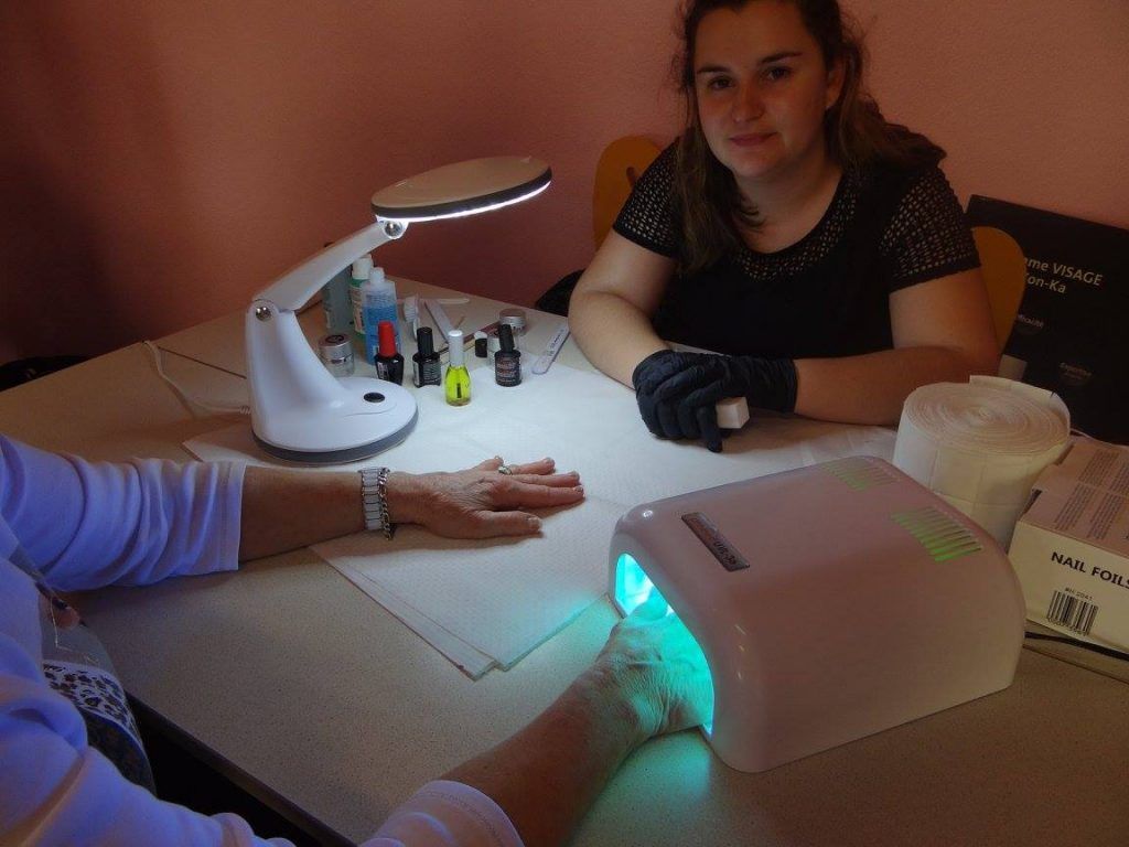 Une femme réalise une manucure. Main sous lampe UV. Table avec lampe et matériel de manucure.