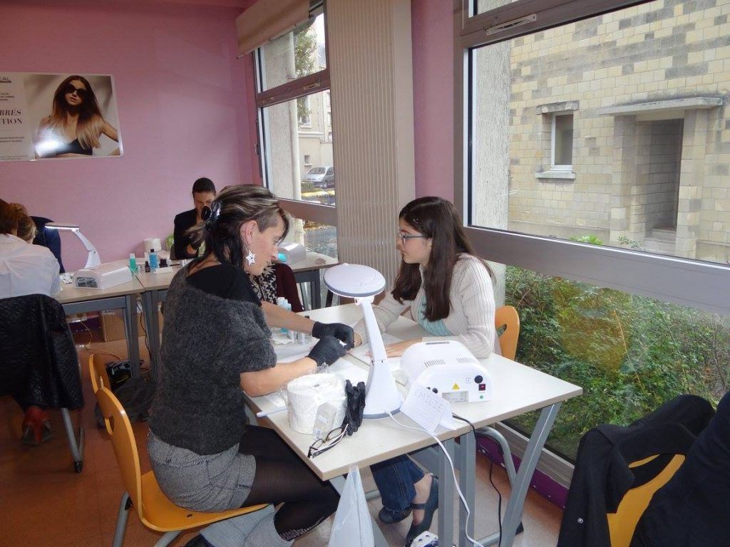 Des personnes assises à une table se font faire une manucure dans une pièce lumineuse avec une grande fenêtre.