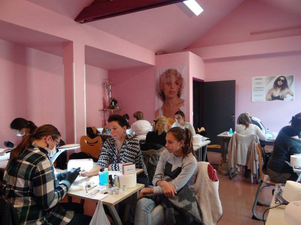 Une pièce où des personnes se font faire des manucures à de petites tables. Murs roses.