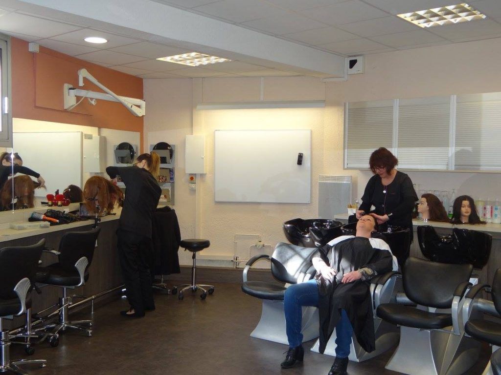 Intérieur d'un salon de coiffure : une personne se fait laver les cheveux ; un coiffeur et des têtes de mannequin sont présents.