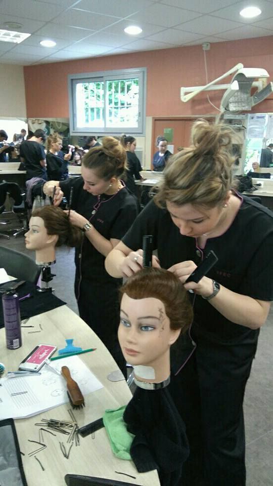 Des élèves coiffeurs s'exercent à coiffer des têtes de mannequins en salle de classe.