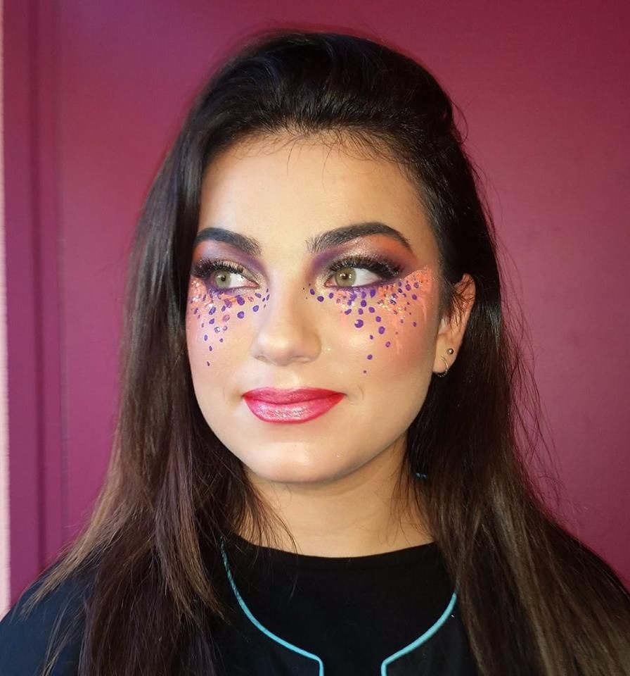 Femme au maquillage sophistiqué des yeux et aux joues maquillées de points, sur fond rose.