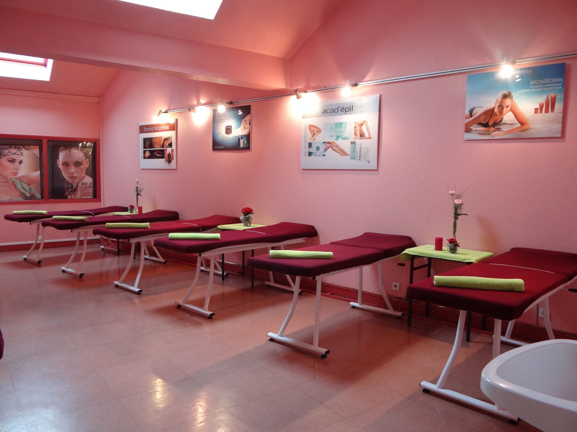 Salle de spa rose avec tables de massage, affiches et éclairage tamisé.