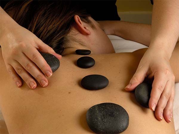 Des mains posant des pierres chaudes sur le dos d'une personne lors d'un massage.