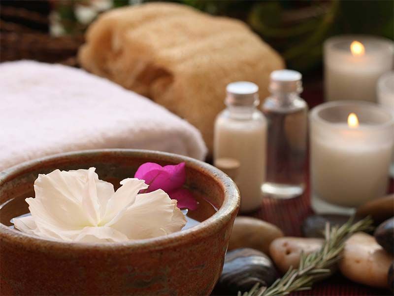 Aménagement spa avec un bol d'eau et des pétales de fleurs, des bougies, des lotions, une serviette et des pierres.