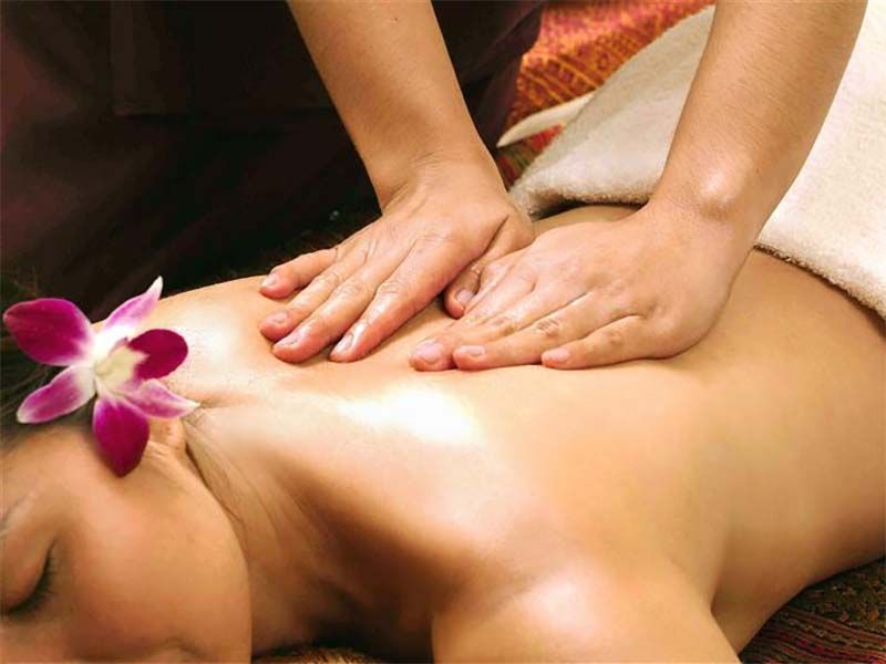 Des mains massent le dos d'une personne. Une fleur repose sur son épaule. Lumière chaude.