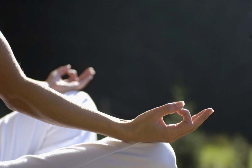 Mains en Jnana mudra, personnage assis vêtu de blanc. Fond sombre avec lumière du soleil.