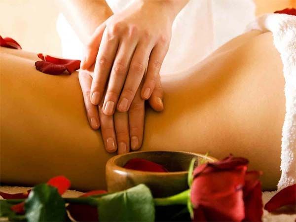 Massage du dos d'une personne avec les mains, des pétales de roses rouges et des fleurs dans un cadre de spa.