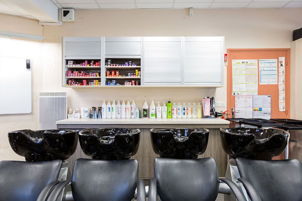 Salon de coiffure avec quatre lavabos noirs, des chaises, des produits et des armoires.