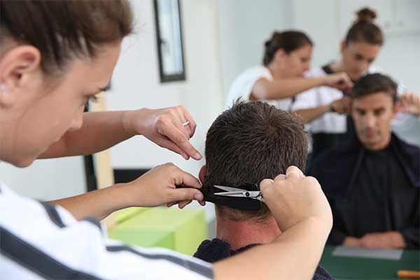 Une coiffeuse coupe les cheveux d'un homme, tandis que d'autres coiffeurs travaillent dans un salon.