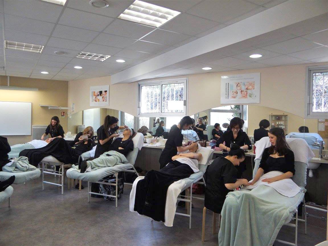 Salle de formation d'esthéticiennes : les élèves réalisent des prestations sur des clientes installées sur des tables de soins.
