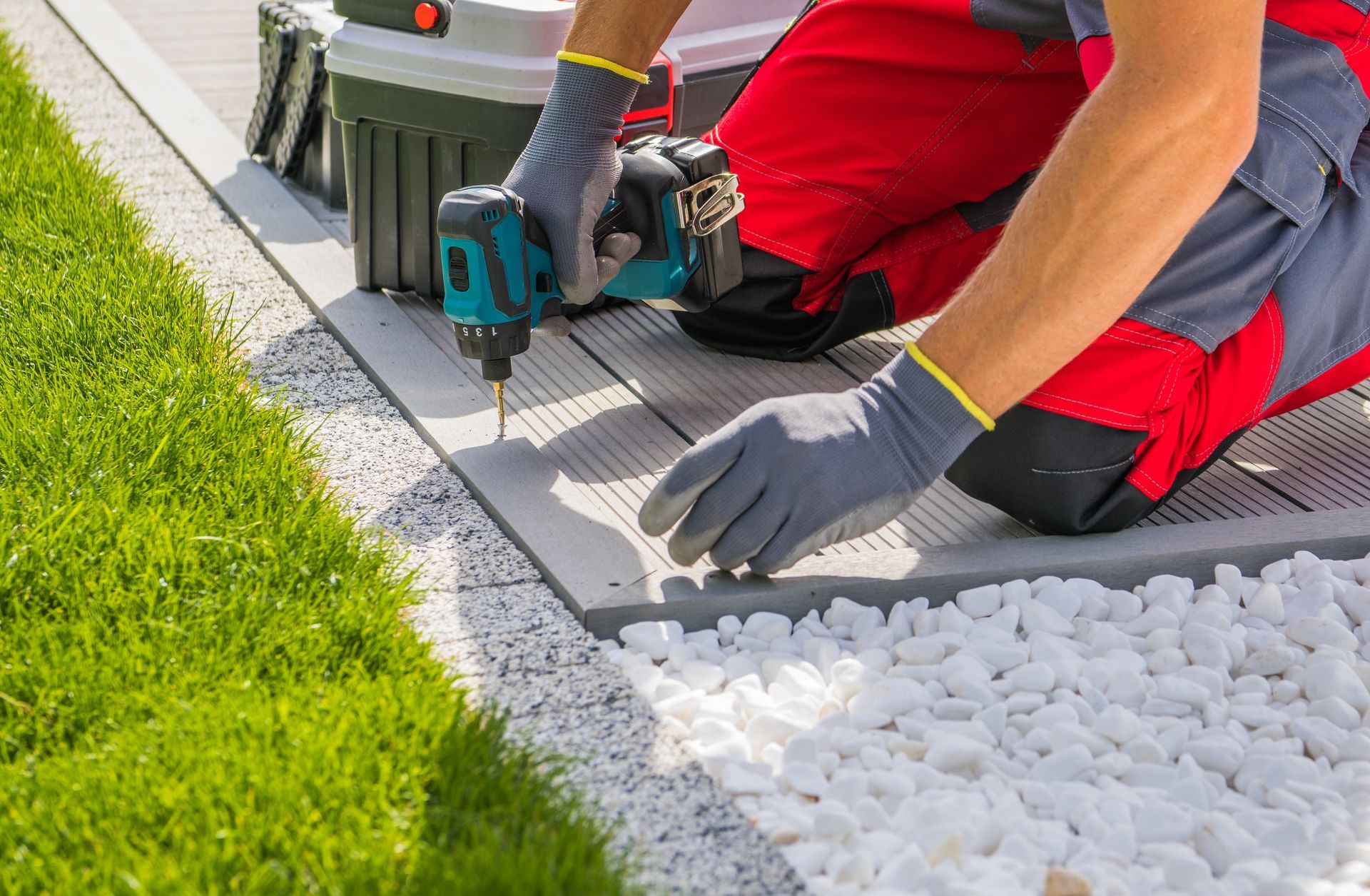 Un ouvrier utilise une perceuse pour installer une bordure entre l’herbe et le gravier blanc d’une allée de jardin