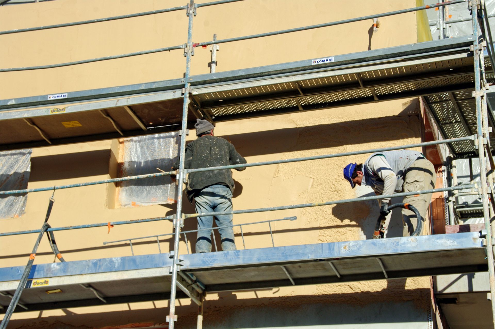 Des ouvriers sur un échafaudage réparent la façade d’un bâtiment à l’aide d’outils à enduire