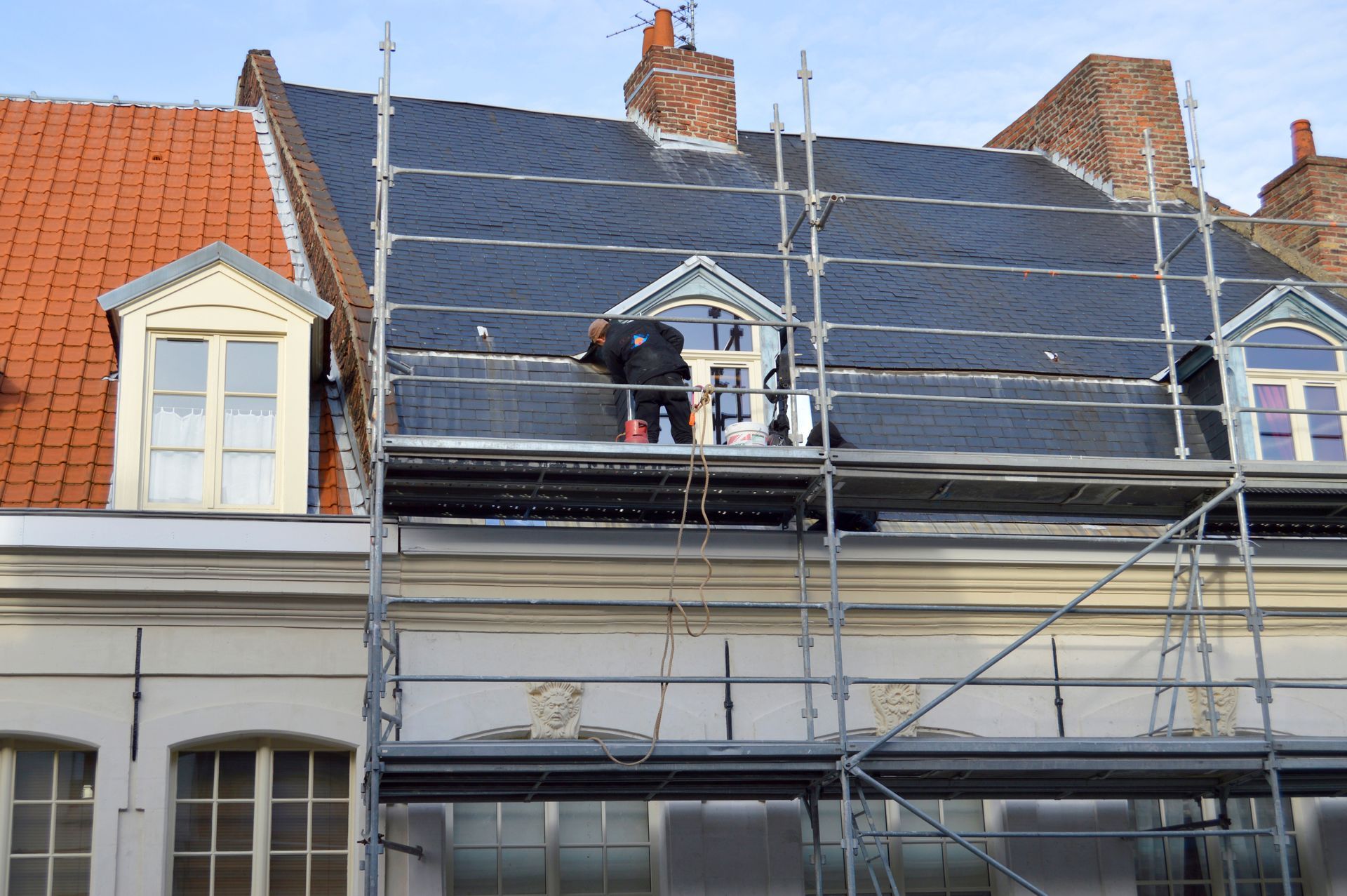 Des ouvriers sur un échafaudage installent des panneaux solaires sur la façade d’une maison au toit rouge