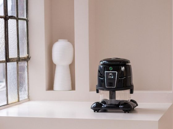 A black vacuum cleaner is sitting on a white counter next to a window.
