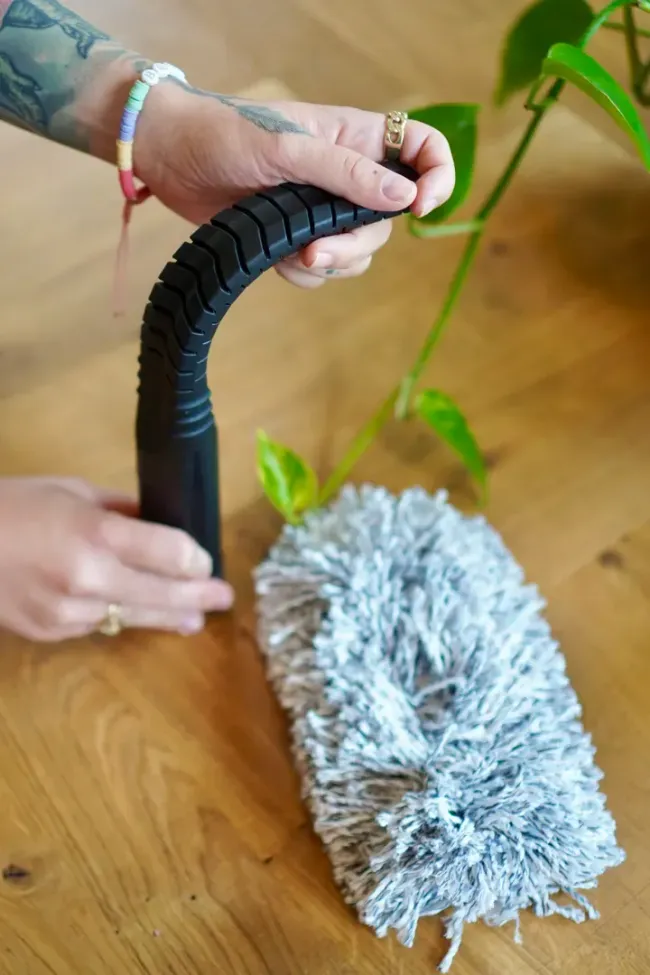 A person is holding a duster on a wooden table.