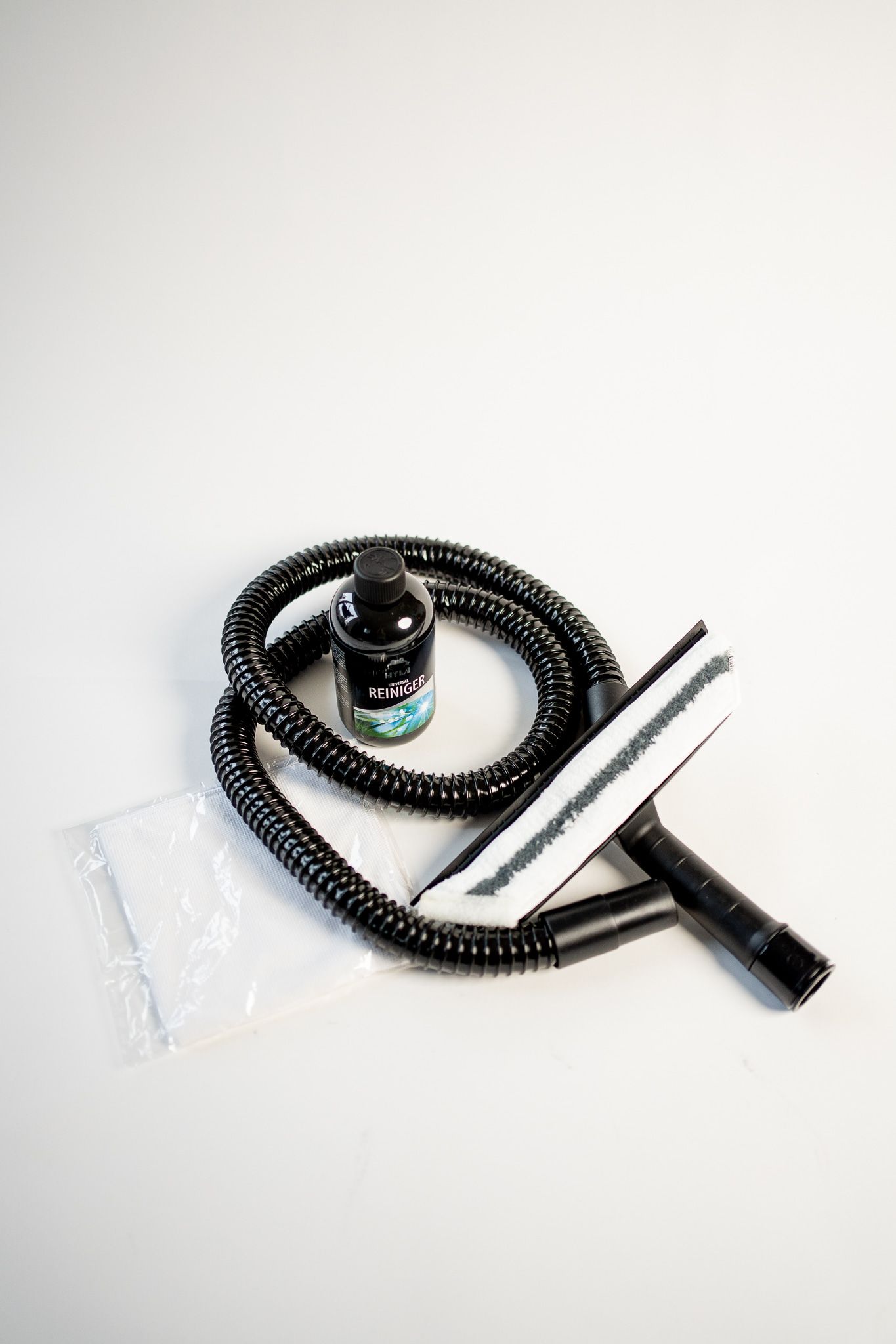 A vacuum cleaner with a hose , brush , and bottle on a white surface.