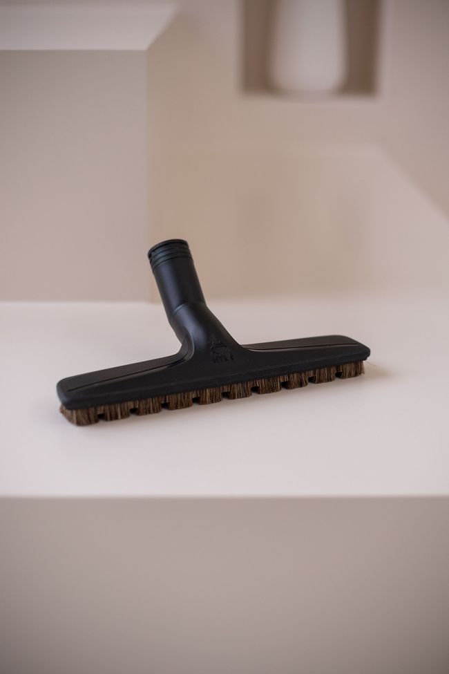 A black vacuum cleaner brush is sitting on top of a white table.