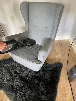 A person is cleaning a chair with a vacuum cleaner.