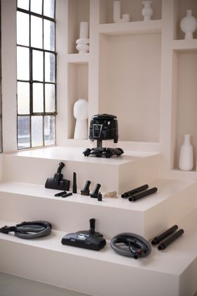 A vacuum cleaner is sitting on top of a white shelf next to a window.