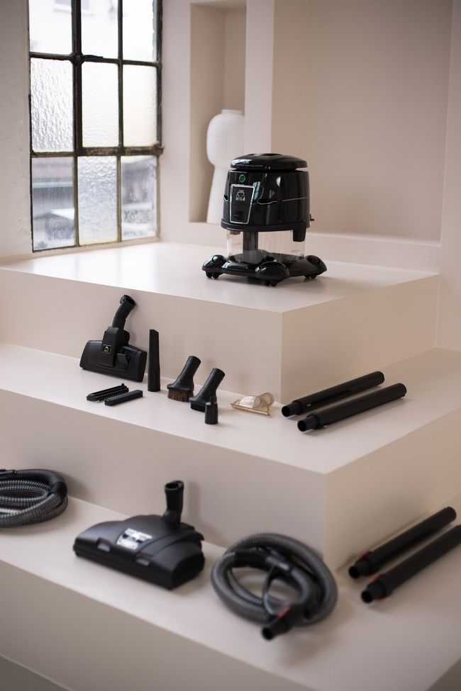 A vacuum cleaner is sitting on top of a white shelf next to a window.