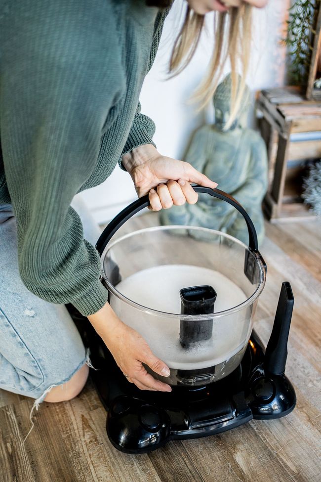 A woman is cleaning a vacuum cleaner on the floor.