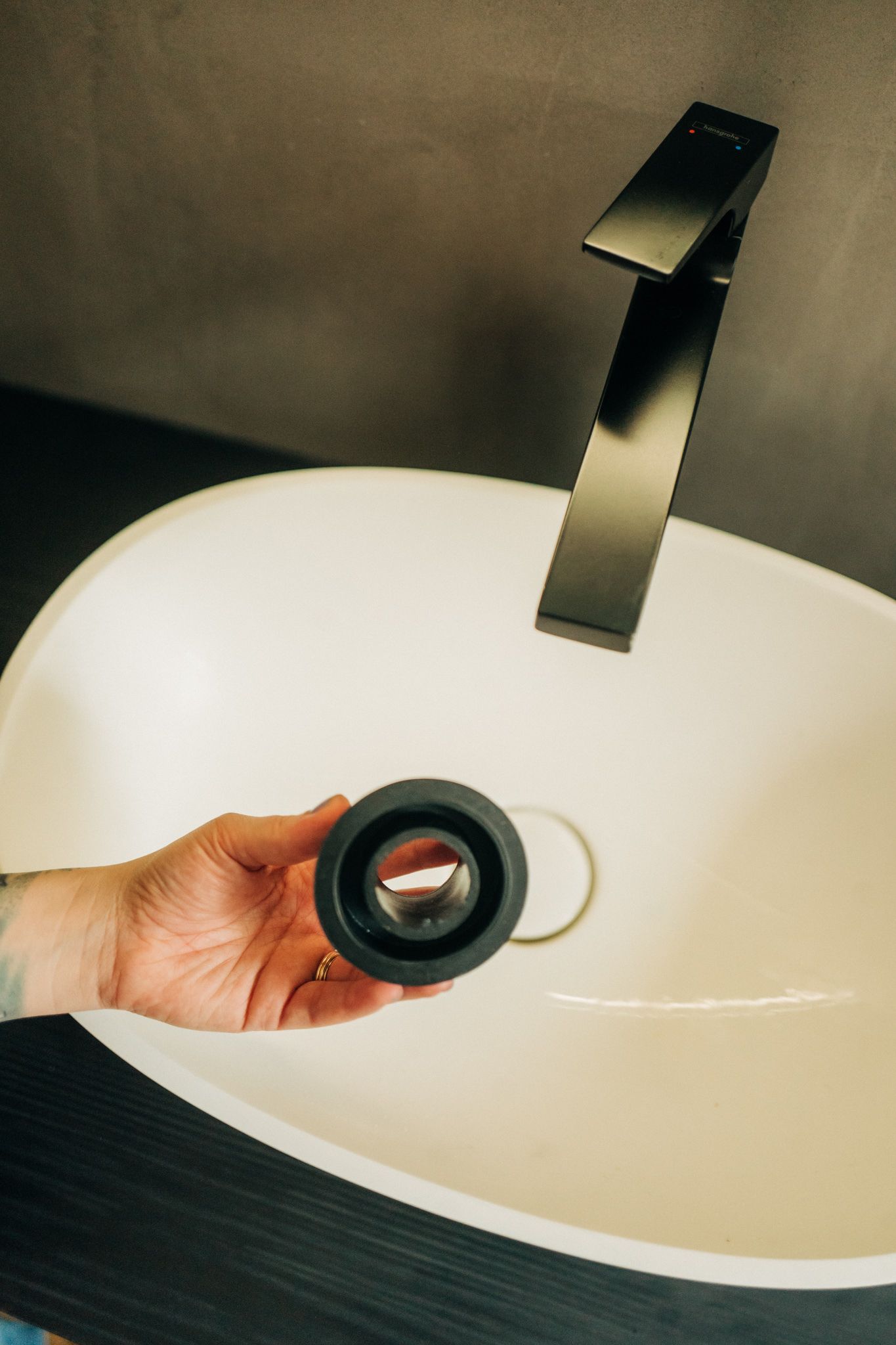 A person is holding a drain plug in front of a sink.