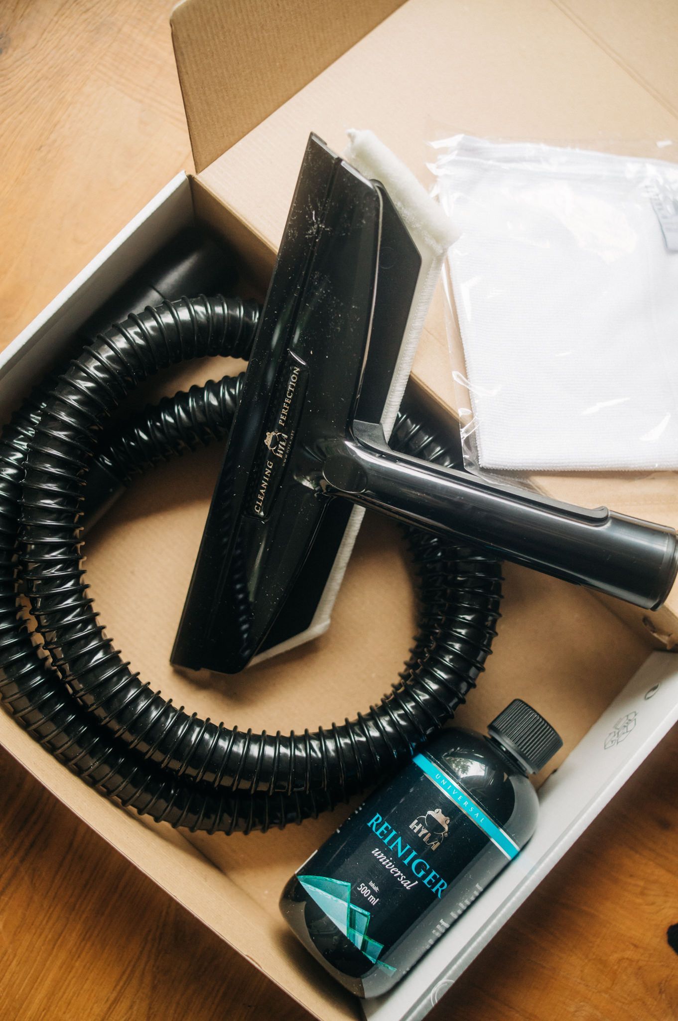 A vacuum cleaner is in a box with a hose and a bottle of cleaner.