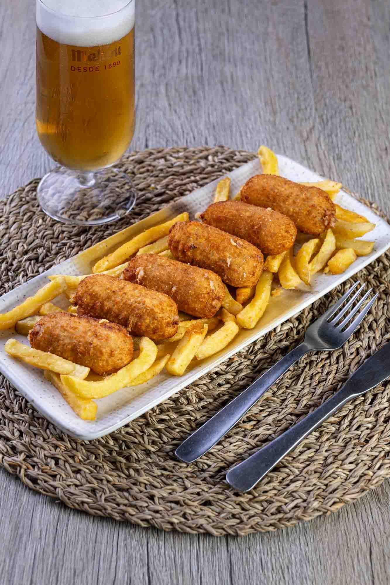Un plato de comida con patatas fritas y un vaso de cerveza en una mesa.