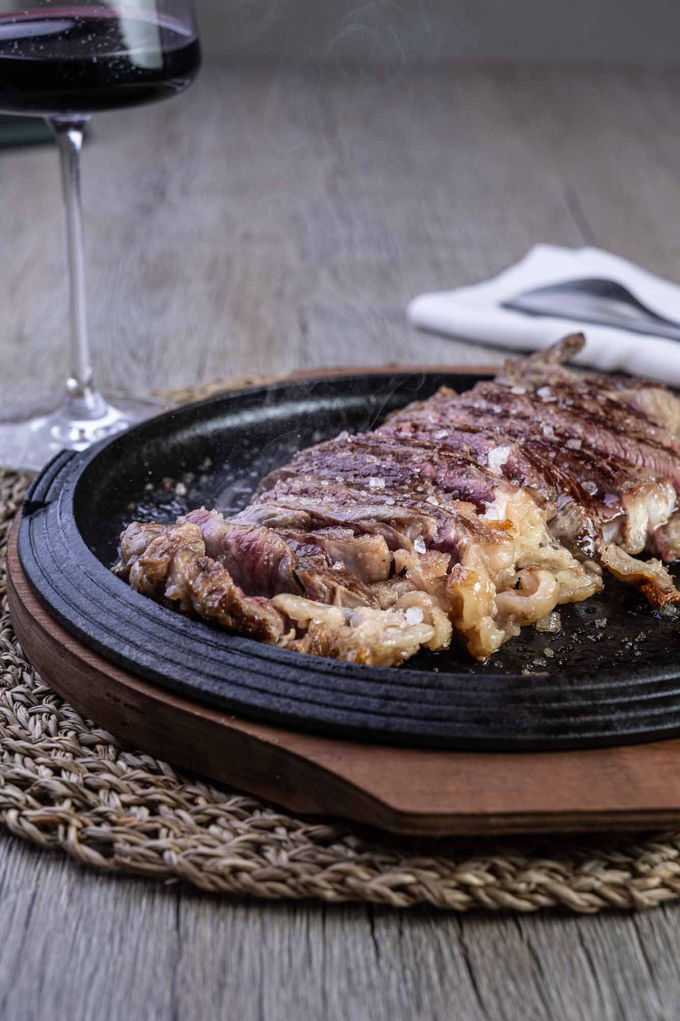 Un filete está en un plato al lado de una copa de vino.