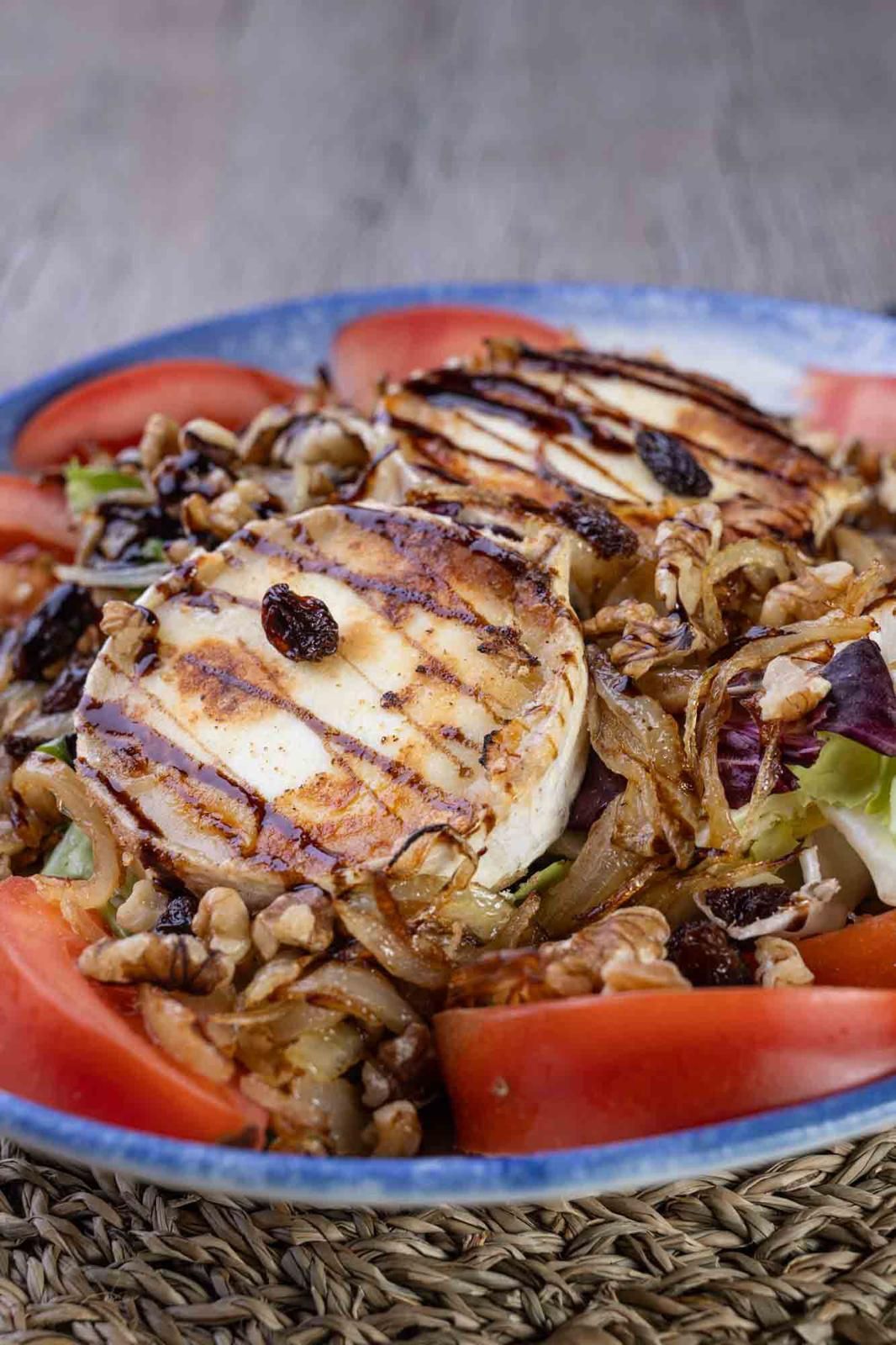 Un primer plano de una ensalada con queso a la parrilla, tomates, nueces y pasas en un plato.