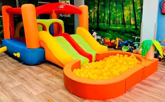 Manos de niños en un recipiente amarillo lleno de perlas de gel verdes y transparentes, con mangas verdes, sobre una superficie azul.