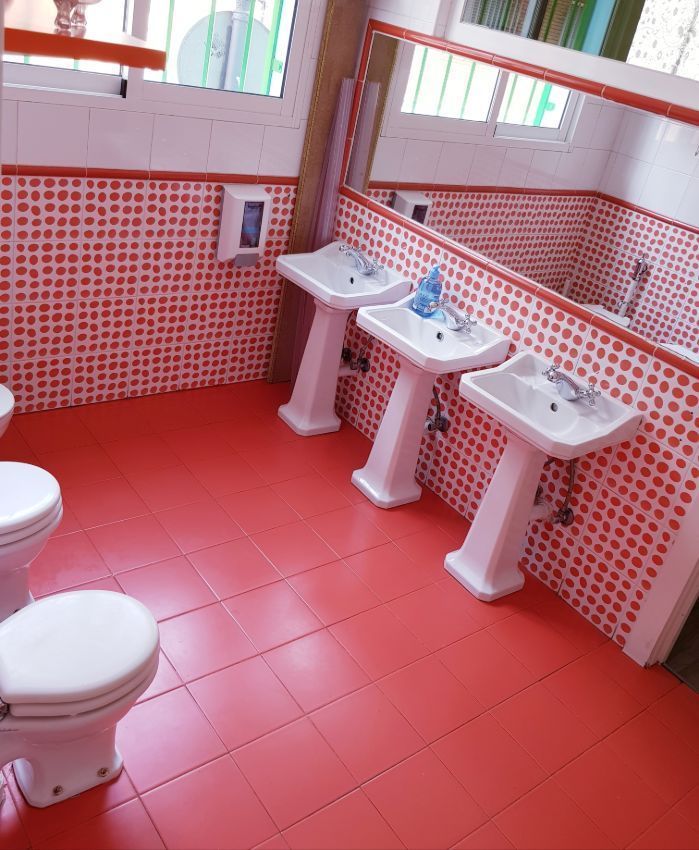 Baño con azulejos rojos, tres lavabos e inodoros.