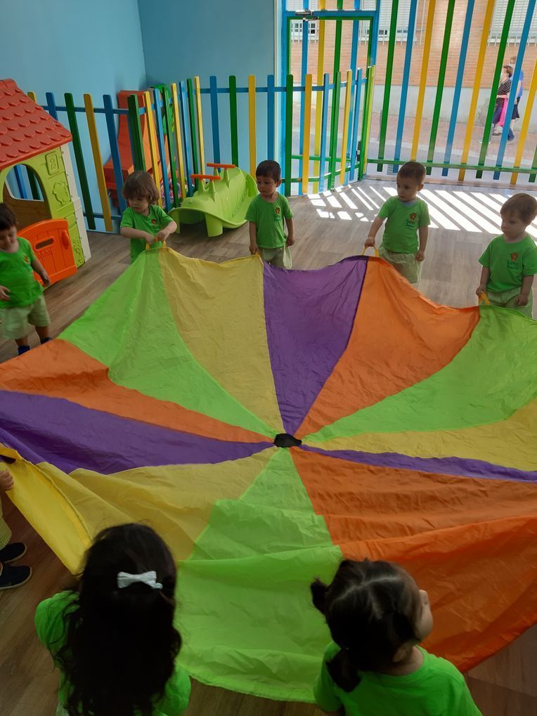 niños jugando con un circulo en tela de colores